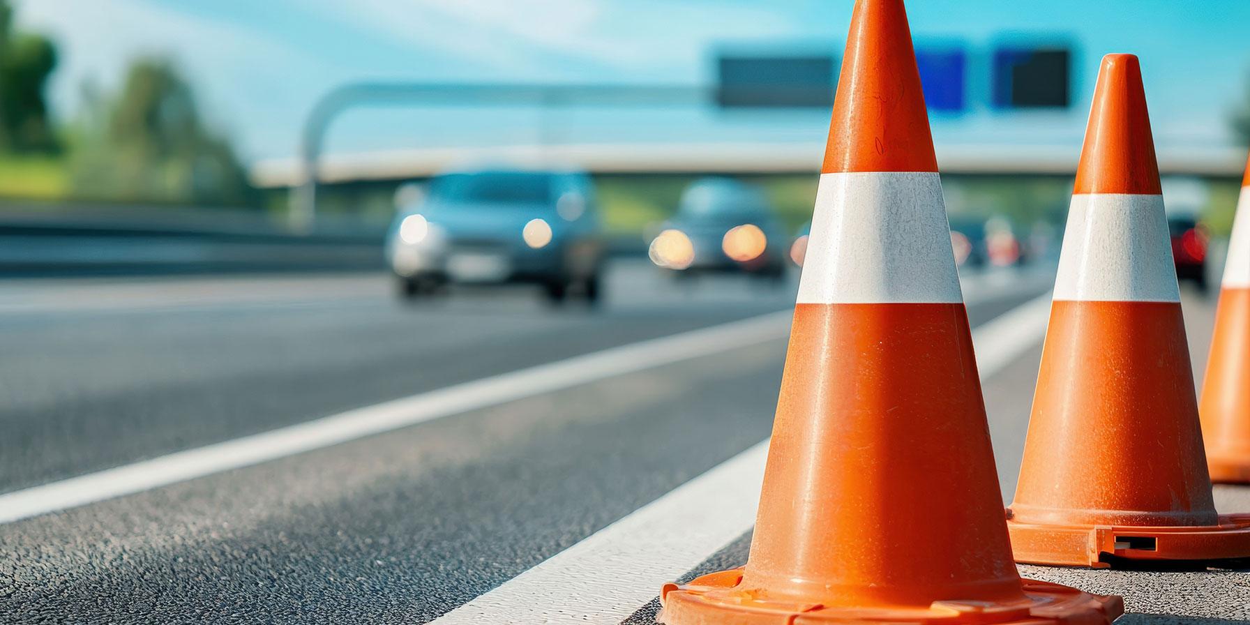 Focus on closeup of orange road cones with cars in background