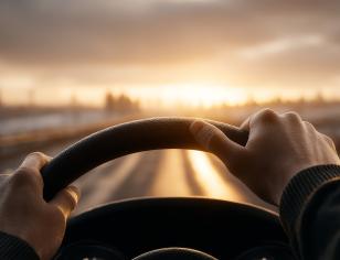 hands on steering wheel driving on road at dusk